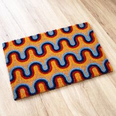 an orange, blue and red rug sitting on top of a wooden floor next to a wood floor