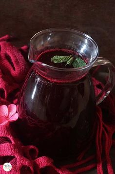 a pitcher filled with liquid sitting on top of a red blanket next to a pink flower