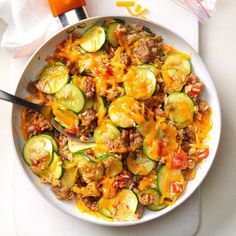 a white bowl filled with zucchini and meat covered in cheese on top of a table