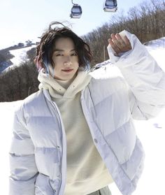 a woman standing in the snow wearing a jacket and holding her hands behind her head