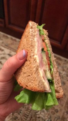 a hand holding a sandwich with lettuce and meat on it in front of a counter