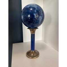 a blue glass ball sitting on top of a metal stand next to a white wall