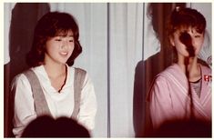 two young women standing next to each other in front of a wall with curtains on it