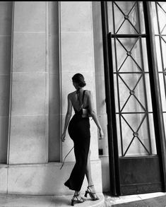 black and white photograph of woman in evening dress leaning against wall with hand on hip