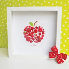 an apple made out of buttons in a white frame with a red bow on the side