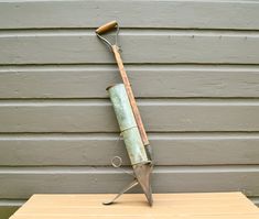 an old rusty garden tool sitting on top of a wooden table next to a gray wall