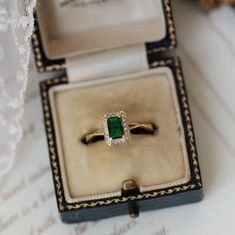 an engagement ring with a green stone sits in a box on a white tablecloth