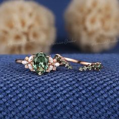 a close up view of a ring with green stones and diamonds on the side, sitting on a blue surface