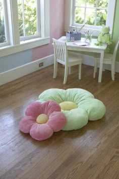 three flower shaped pillows on the floor in front of a table and chair with pink walls