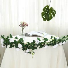 the table is covered with white flowers and greenery, along with an open book