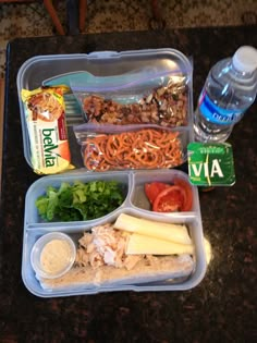 a plastic container filled with food on top of a table next to a bottle of water