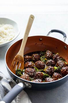 meatballs and broccoli are being cooked in a pan with a wooden spoon