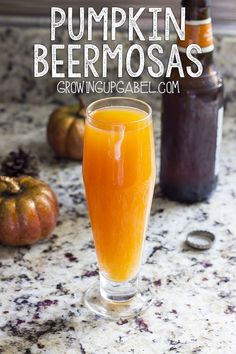 a glass filled with orange juice next to two pumpkins and bottles on the counter