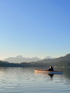 a person in a kayak paddling on the water with mountains in the background