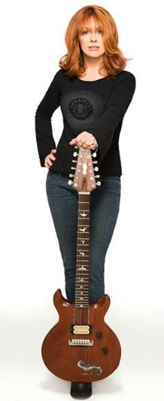 a woman standing on top of a guitar with her hands on the back of it