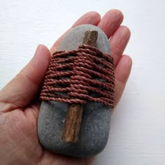 a hand holding a rock with a wooden cross on it and rope wrapped around it