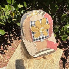 a woman wearing a hat with flowers on it sitting in front of some bushes and trees