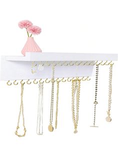 a white shelf with lots of necklaces and a pink flower in a vase on top