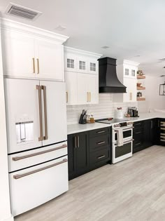 a kitchen with black and white cabinets, wood flooring and stainless steel range hood