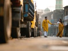 a man and woman walking down the street holding hands with trucks in the back ground