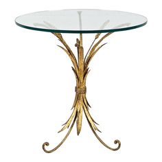 a glass and metal table with gold leaf design on the top, against a white background