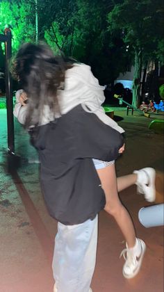 a woman in white shorts and black jacket holding onto another woman's back as they walk through the park at night