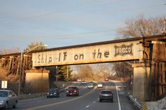 cars drive under an old bridge that reads sit - it on the frisbee