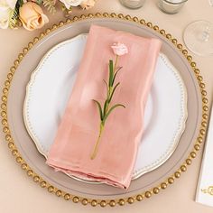 a place setting with pink napkins and flowers on the plate, along with silverware