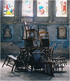 many chairs are stacked up in front of stained glass windows