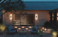 an outdoor living area with lights on the walls and couches in the graveled area