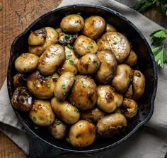 a skillet filled with mushrooms on top of a wooden table next to parsley