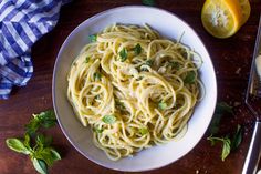 a white bowl filled with pasta and garnished with parsley next to lemon wedges