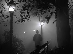 a man is walking down the stairs in the foggy night with his hat on