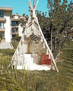 a teepee sitting in the grass next to some bushes and trees with a building in the background