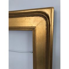 an old gold frame hanging on the wall next to a white wall with a cord in it