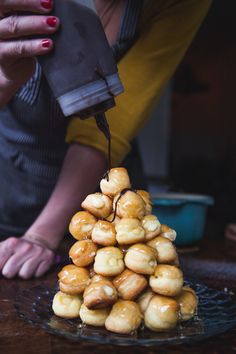 a woman is pouring syrup on some donuts in the shape of a pyramid,