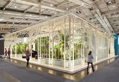 people are walking around in an indoor garden showroom with white walls and glass windows