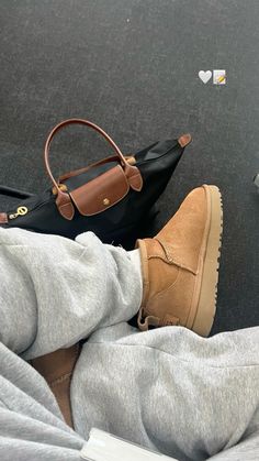 a person's feet in grey sweatpants and brown shoes with a purse on the ground