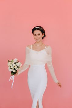 a woman in a white dress is holding a bouquet and posing for a photo against a pink background