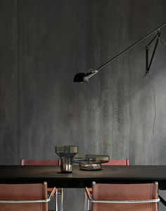 a table with two chairs and a lamp on top of it in front of a gray wall