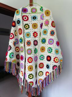 a crocheted granny blanket hanging on a clothes hanger with tassels