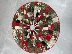 a red and green quilted table top on the floor in a circle with christmas decorations