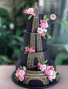 a three tiered black cake with pink flowers on the bottom and gold trimmings