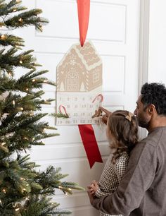 a man and woman are decorating a christmas tree with a house ornament