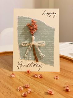 a happy birthday card with flowers on top of a wooden table next to some petals