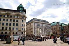 many people are walking around in an old city square with tall buildings and green domes