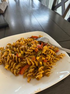 a white plate topped with pasta covered in sauce and vegetables next to a fork on top of a wooden table