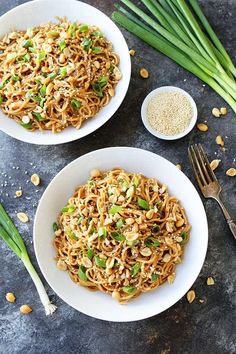 two white bowls filled with noodles and green onions next to some chopsticks on a table