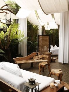 an outdoor seating area with white drapes on the ceiling and wooden furniture in the middle