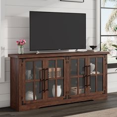 a large flat screen tv mounted on top of a wooden entertainment center with glass doors